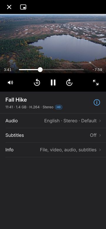The Hi, bye player on iPhone playing Fall Hike, an aerial view of an autumn lake, with audio, subtitle and info options below.